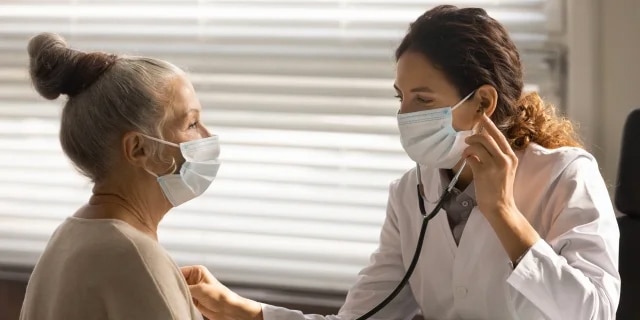 masked patient with masked doctor as she examines her hear
